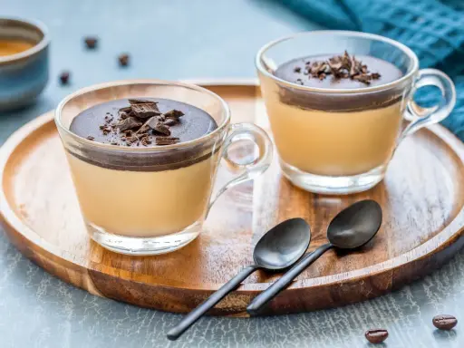 Delizioso semifreddo al caffè con copertura al cioccolato e scaglie croccanti, servito in coppette di vetro su un vassoio di legno.