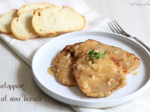 Tre scaloppine al vino bianco su un piatto bianco, guarnite con timo fresco, accompagnate da fette di pane tostato.