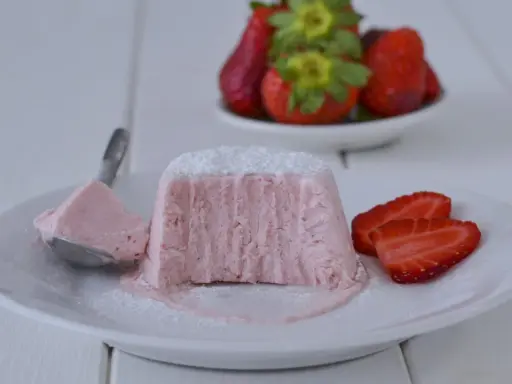 Delizioso semifreddo alle fragole, con una fetta servita su un cucchiaino e guarnito con zucchero a velo e fragole fresche.