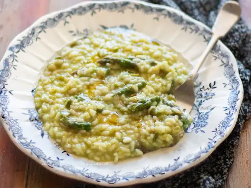 Un cremoso risotto con asparagi, servito in un piatto decorato. Un piatto primaverile che profuma di buono.
