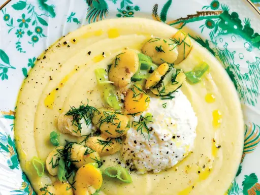 Un cremoso macco di fave fresche, guarnito con ricotta, fave intere, cipollotto e aneto, servito su un piatto decorato.