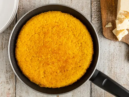 Un invitante riso al salto dorato in padella, pronto per essere gustato con scaglie di Parmigiano Reggiano.