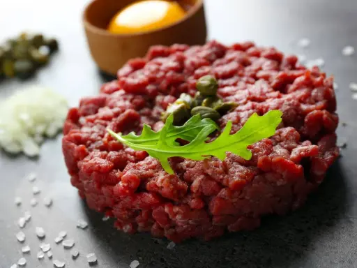 Tartare di manzo fresca, guarnita con capperi e rucola, pronta per essere gustata con tuorlo d'uovo e cipolla.
