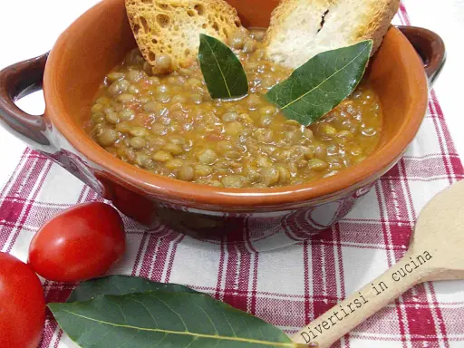 Un piatto fumante di lenticchie in umido, guarnito con crostini e foglie di alloro, pronto per essere gustato.