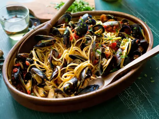 Un invitante piatto di spaghetti con le cozze, condito con pomodoro e prezzemolo, pronto per essere gustato.
