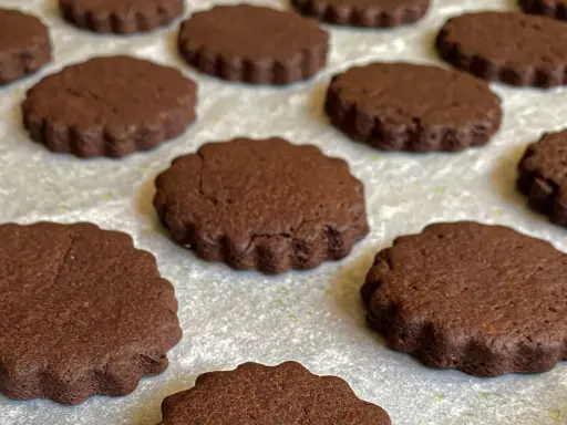 Deliziosi biscotti senza burro al cacao, con bordo ondulato, disposti su una teglia.