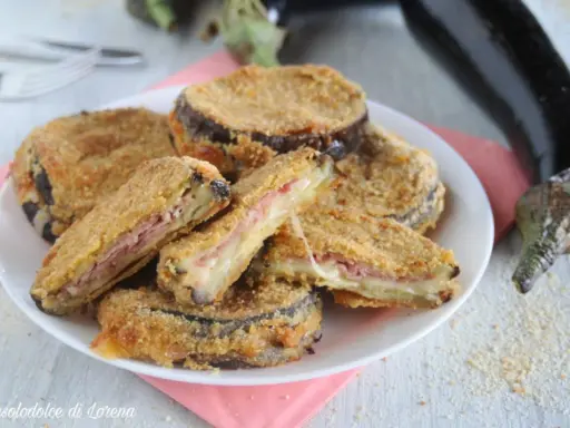 Cordon bleu di melanzane impanati e fritti, ripieni di prosciutto e formaggio filante, serviti su un piatto bianco.