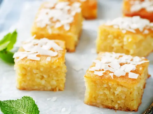 Deliziosi quadretti di torta al cocco, guarniti con scaglie di cocco e foglioline di menta fresca.