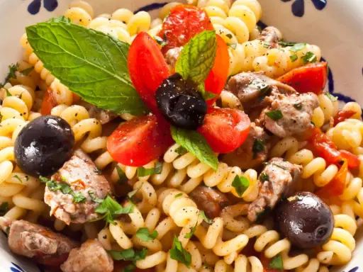 Pasta con pesce spada, pomodorini, olive nere e menta fresca in una ciotola decorata.