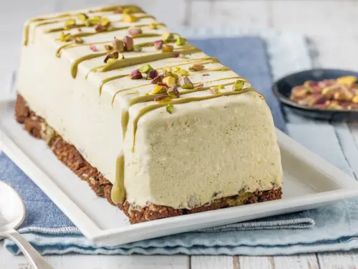 Semifreddo al pistacchio, un dolce gelato decorato con glassa verde e granella di pistacchi, su una base croccante.