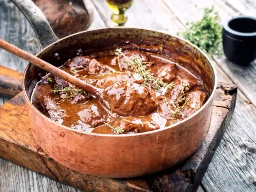Un saporito brasato di manzo, cotto lentamente in una pentola di rame, guarnito con timo fresco.