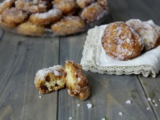 Frittelle di riso ricetta della nonna: dolcetti dorati e zuccherati, alcuni su un piatto, altri su un pizzo, uno aperto rivela l'interno morbido.