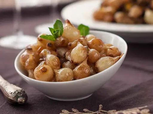 Ciotola di cipolle in agrodolce caramellate, guarnite con menta fresca.