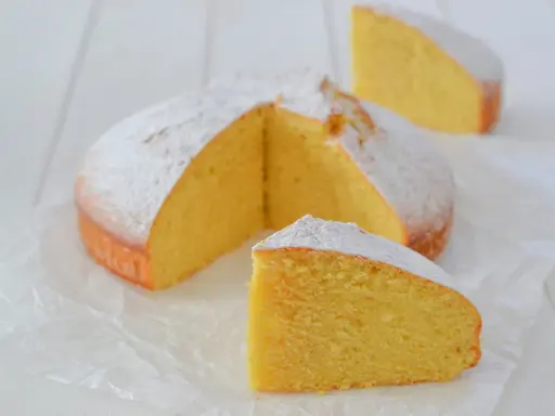 A fluffy lemon cake dusted with powdered sugar, with two slices cut out.