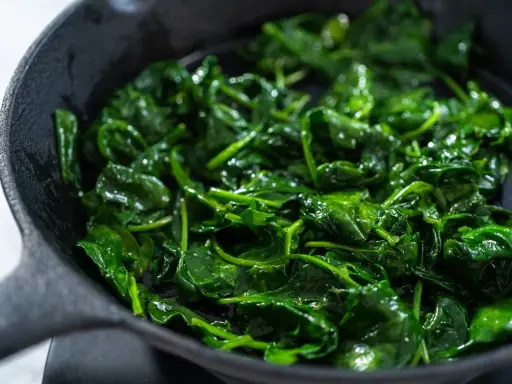 Spinaci freschi e lucidi che sfrigolano in una padella di ghisa, pronti per essere gustati.