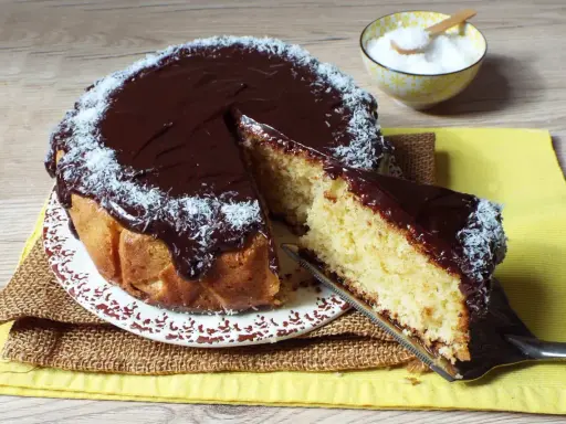 Deliziosa torta cocco e cioccolato, con una fetta appena tagliata e cosparsa di cocco grattugiato.
