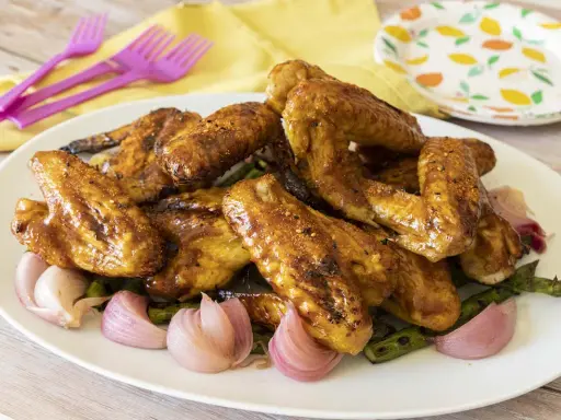 Alette di pollo in padella, dorate e succulente, servite con cipolle rosse e asparagi su un piatto bianco.