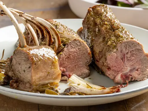 Costolette di agnello al forno succulente, condite con erbe aromatiche, servite su un piatto con verdure arrosto.
