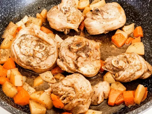 Porzioni di ossobuco di tacchino cotte in padella con patate e carote a cubetti, condite con erbe aromatiche.