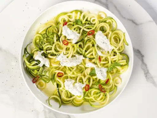 Spaghetti di zucchine freschi con ricotta cremosa, peperoncino e menta, un piatto leggero e colorato.