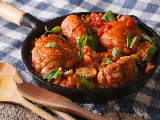 Pezzi di coniglio alla cacciatora in padella con pomodoro, olive e basilico, pronti per essere gustati.