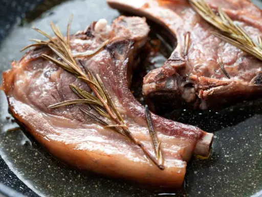 Due braciole di maiale succulente cuociono in padella con rametti di rosmarino.