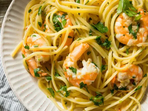 Un piatto invitante di pasta con gamberetti, condita con prezzemolo fresco e servita su un piatto bianco.