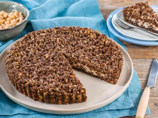 Sbriciolata ricotta e cioccolato con croccante copertura di nocciole. Una fetta è già servita su un piattino.