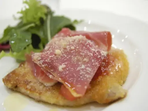 Cotoletta alla bolognese dorata, coperta da prosciutto crudo e parmigiano, con un contorno di insalata fresca.