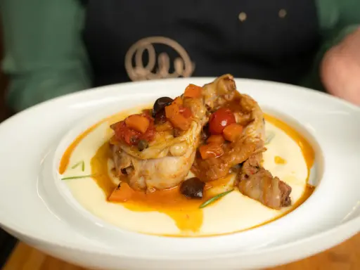Pollo alla cacciatora ricetta della nonna: succulenti pezzi di pollo in umido con pomodoro, olive e carote, serviti su un letto di polenta cremosa.