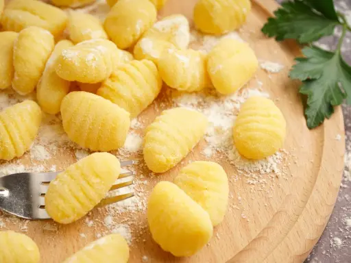 Gnocchi fatti in casa pronti per la friggitrice ad aria, spolverati di farina su un tagliere di legno.