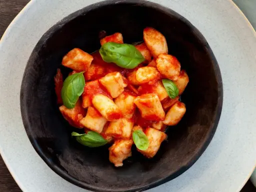 Gnocchi di ricotta soffici e saporiti, conditi con un sugo di pomodoro fresco e guarniti con foglie di basilico.