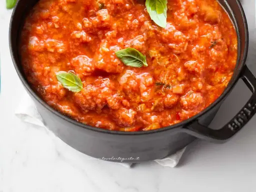 Pappa al pomodoro fumante in una pentola nera, guarnita con foglie di basilico fresco. Un classico piatto toscano.