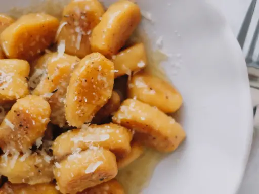 Gnocchi di zucca dorati, conditi con burro fuso, pepe nero e scaglie di parmigiano, pronti per essere gustati.