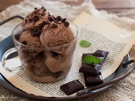Coppa di gelato al cioccolato con scaglie di cioccolato fondente e foglioline di menta, su un vassoio arrugginito con un libro aperto.