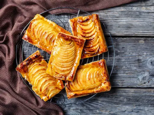 Deliziosi dolci con pasta sfoglia rettangolare, ripieni di mele caramellate, su una griglia di raffreddamento.
