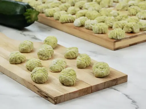 Gnocchi di zucchine freschi, pronti per essere cotti, disposti su taglieri di legno.