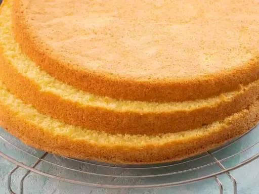 Tre soffici strati di pan di spagna senza glutine raffreddano su una griglia. Un'etichetta con scritto "senza glutine" è appesa alla griglia.