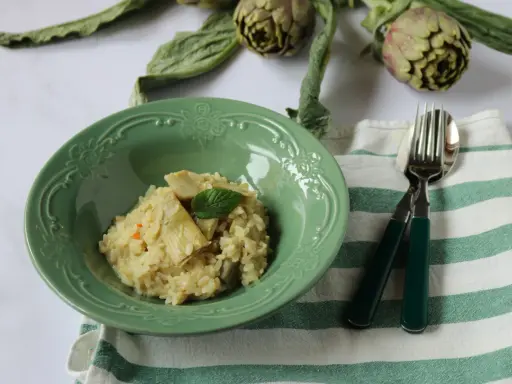 Un cremoso risotto con carciofi freschi, guarnito con una fogliolina di menta, pronto per essere gustato.