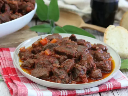 Cinghiale in umido fatto in casa da Benedetta, un piatto ricco e saporito, servito con pane fresco e un bicchiere di vino rosso.