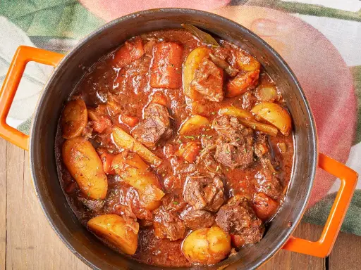 Un saporito spezzatino con patate, cotto lentamente in un tegame arancione, pronto per essere gustato.