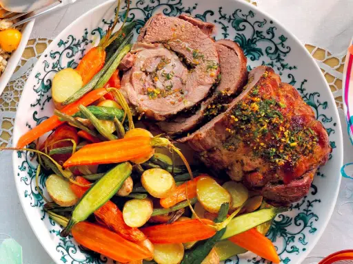 Un succulento agnello al forno, affettato e guarnito con erbe aromatiche, servito con patate novelle, carote e fagiolini.