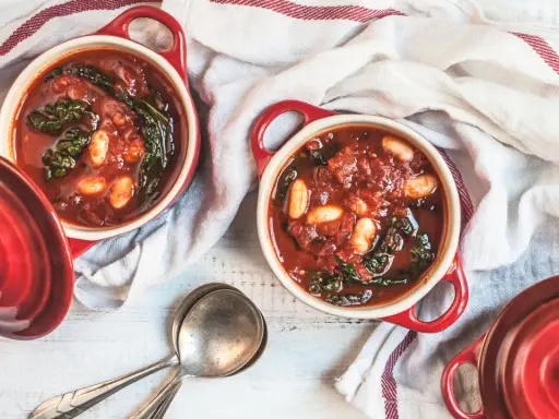Due ciotole rosse con zuppa di cavolo nero e fagioli, pronte per essere gustate.