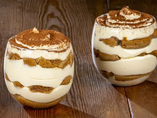 Due bicchieri di delizioso tiramisù senza uova, con strati di savoiardi e crema, spolverati di cacao.