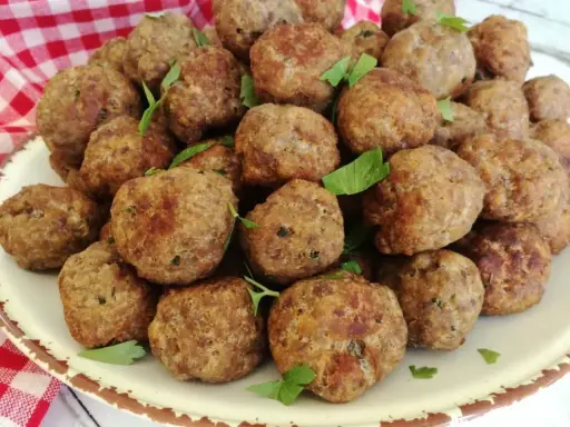 Un piatto colmo di polpette in bianco, dorate e profumate, guarnite con prezzemolo fresco.
