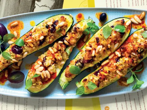 Zucchine ripiene vegetariane, dorate e gustose, guarnite con pinoli, olive e erbe fresche. Un piatto invitante e colorato.