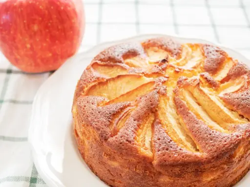 Torta di mele con yogurt, dorata e soffice, con mele a vista. Accanto, una mela rossa fresca.