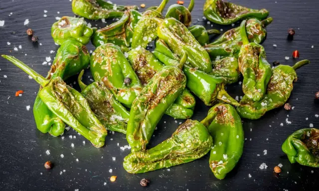 Friggitelli verdi, cotti in friggitrice ad aria, cosparsi di sale grosso e pepe nero su una superficie scura.