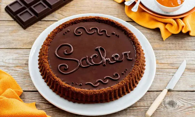 Una crostata morbida al cioccolato, decorata con la scritta "Sacher" in glassa, pronta per essere gustata.