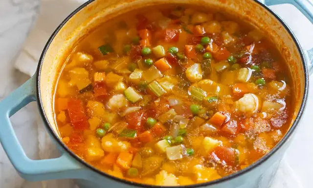 Un fumante minestrone di verdure in una pentola azzurra, ricco di carote, zucchine, piselli e cavolfiore.